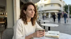 אישה ישראלית יושבת בבית קפה תל-אביבי בבוקר עם קפה ומחברת - איך להתמיד בדיאטה - בריאותלי